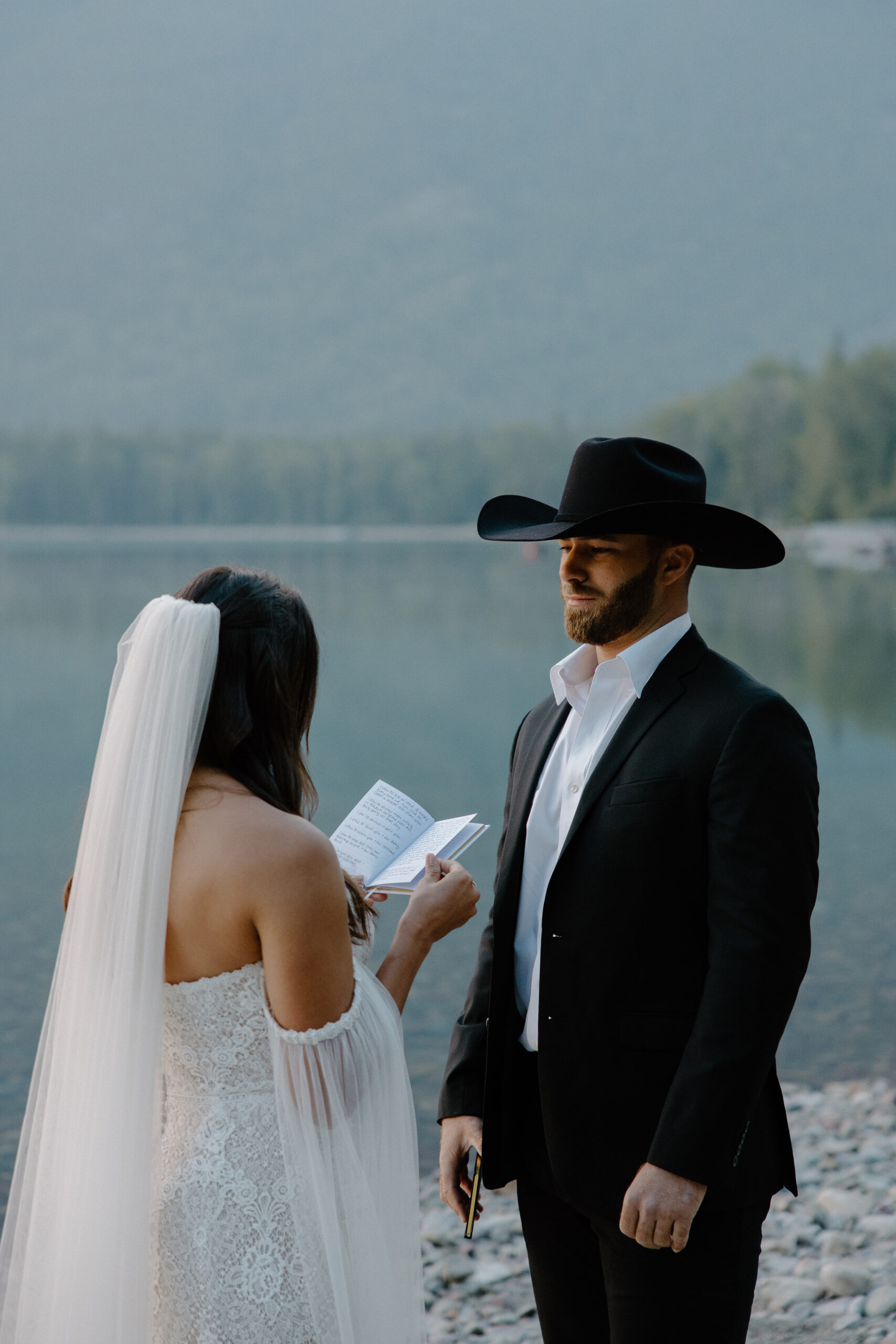 A man looking at his partner as she reads her vows to him during their Glacier National Park wedding over the summer