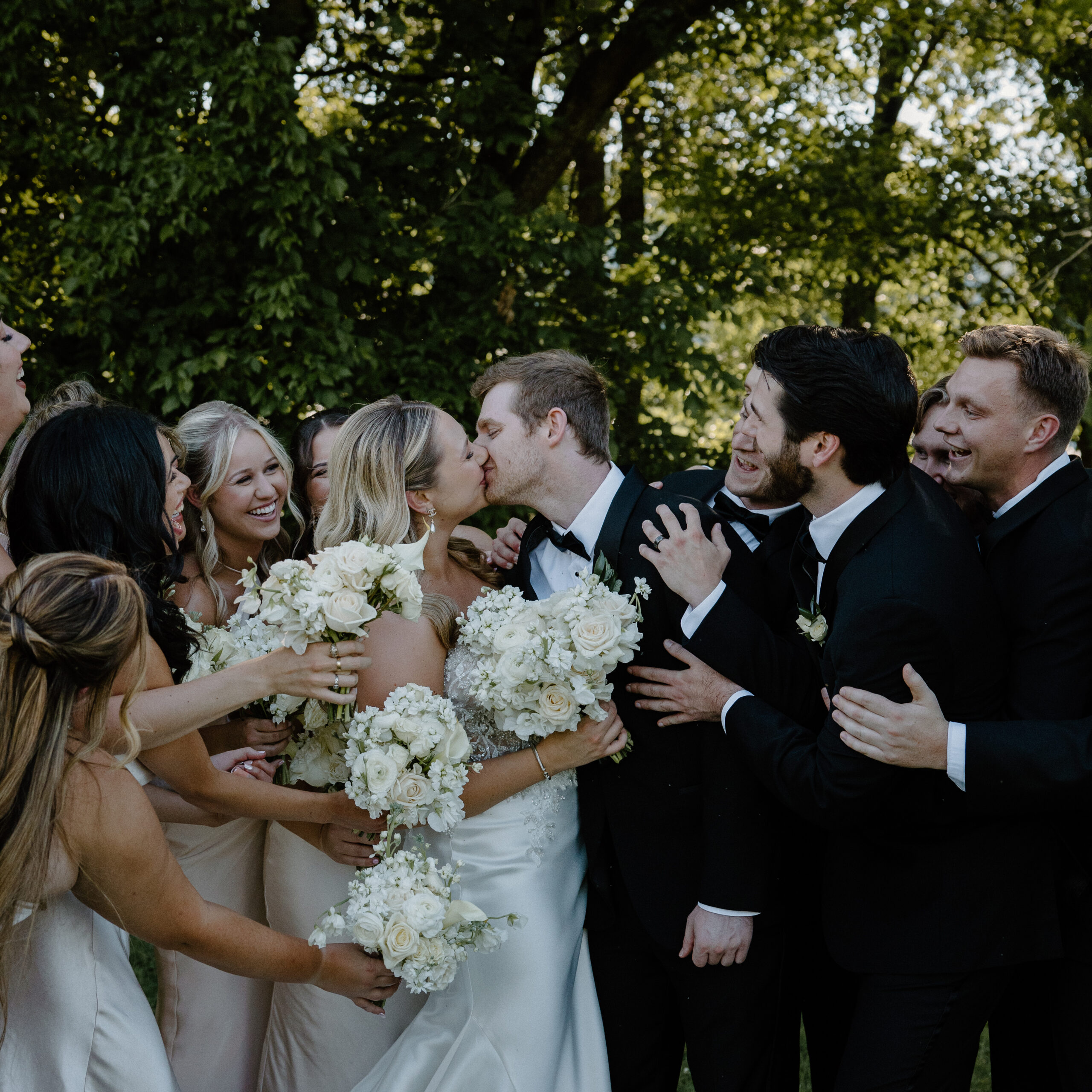 A couple surrounded by their wedding party as they share a kiss during their Diamond Creek Farms wedding