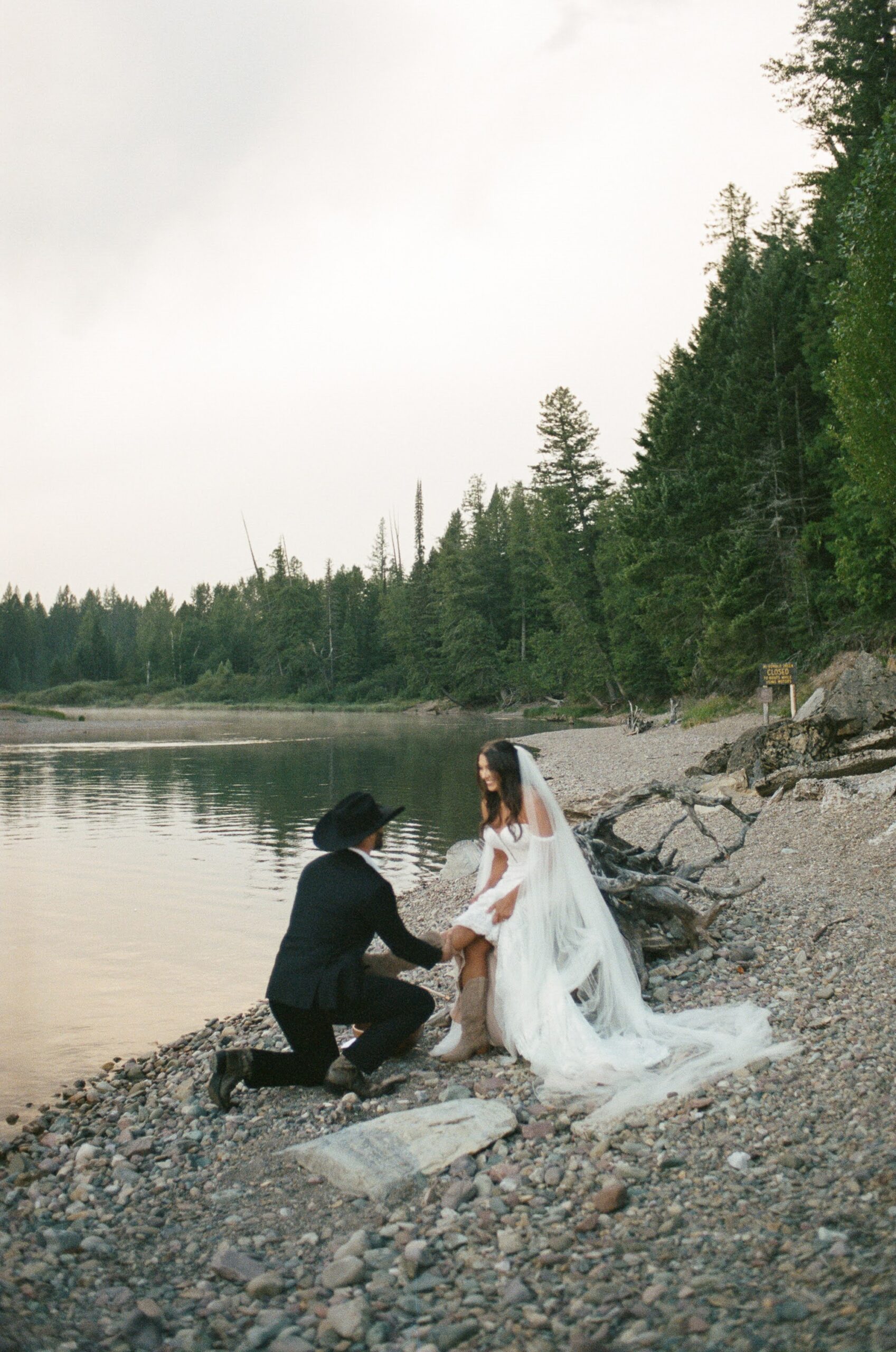 A man washing his partners feet as she sits on a log during their sunrise Glacier National Park elopement
