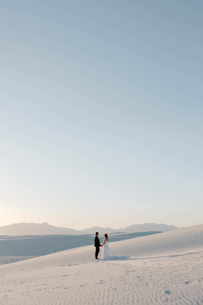 A couple holding hands saying vows to each other as the sun sets during their White Sands National Park elopement in the fall