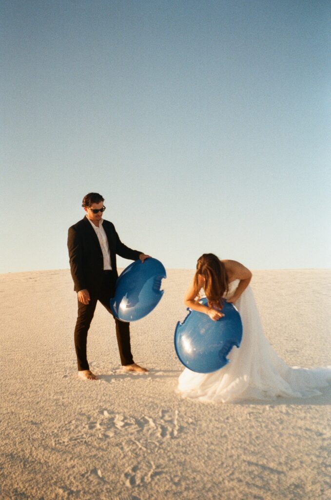 A couple putting wax on their sleds during their White Sands National Park adventure elopement captured on 35 mm film