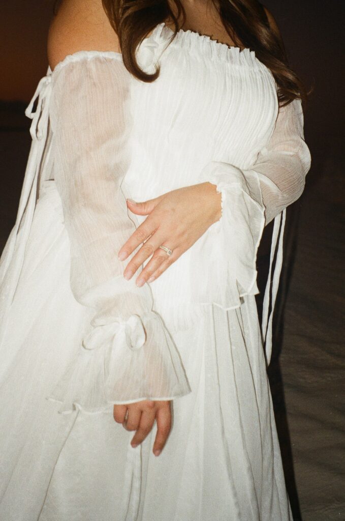 A woman in a strapless wedding dress holding her arm showing off her engagement ring during their southern New Mexico wedding at White Sands National Park captured on 35mm film