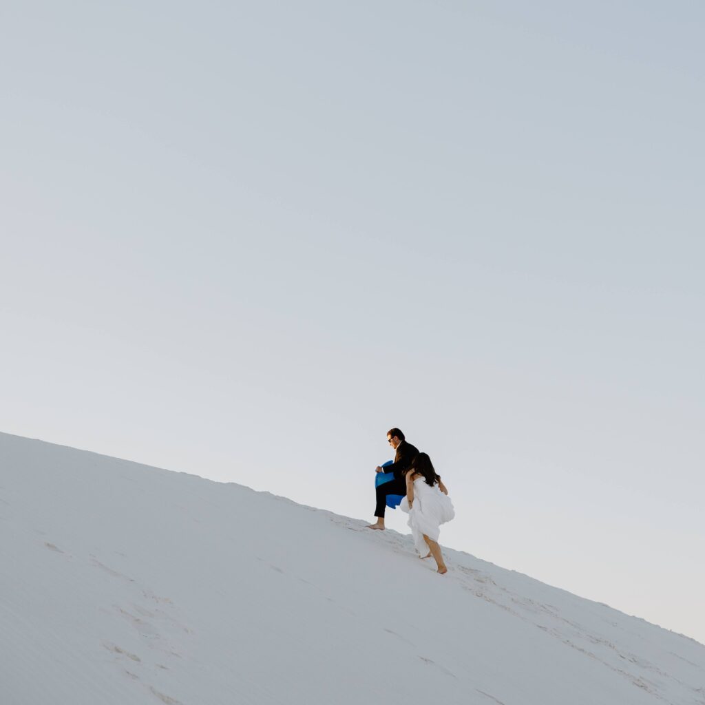 A man leading his partner up the sand dunes as the sun sets on their elopement day in New Mexico