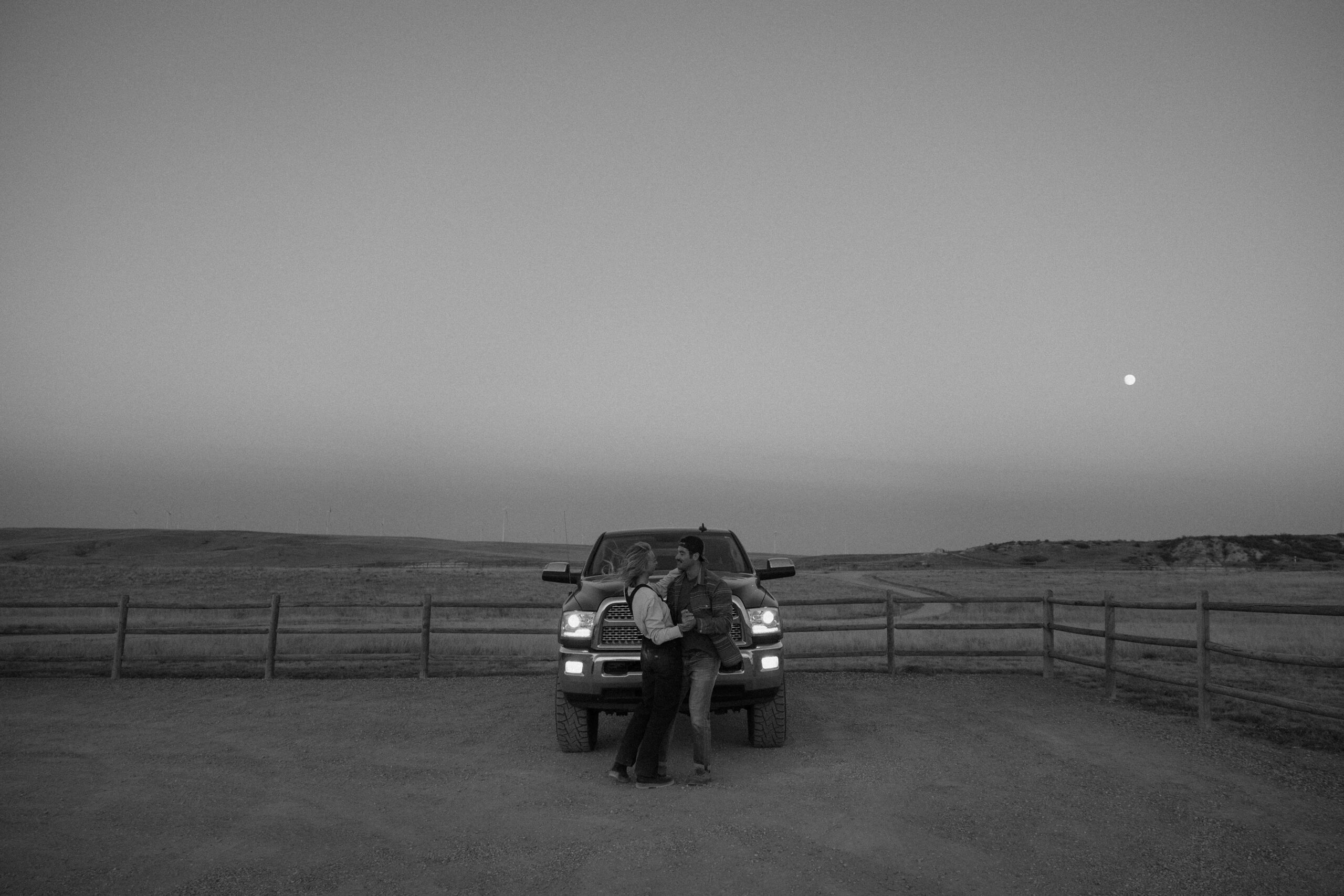 A couple sharing a dance in front of their truck with the headlights on and the moon hanging low in the sky during their Colorado couple photoshoot