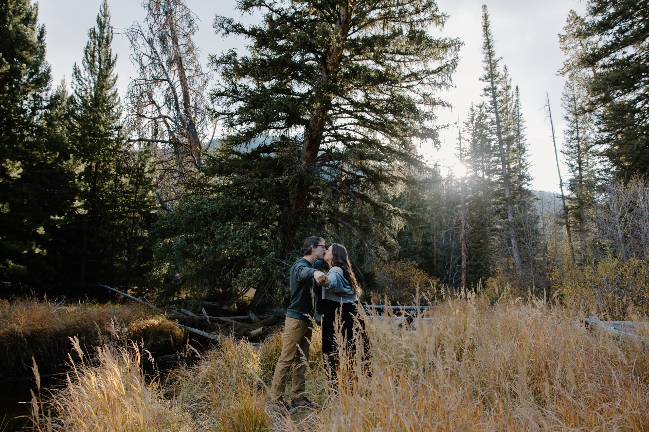 A couple holding hands and swinging into each other to share a kiss as they stand in Rocky Mountain National Park during their Colorado engagement photos