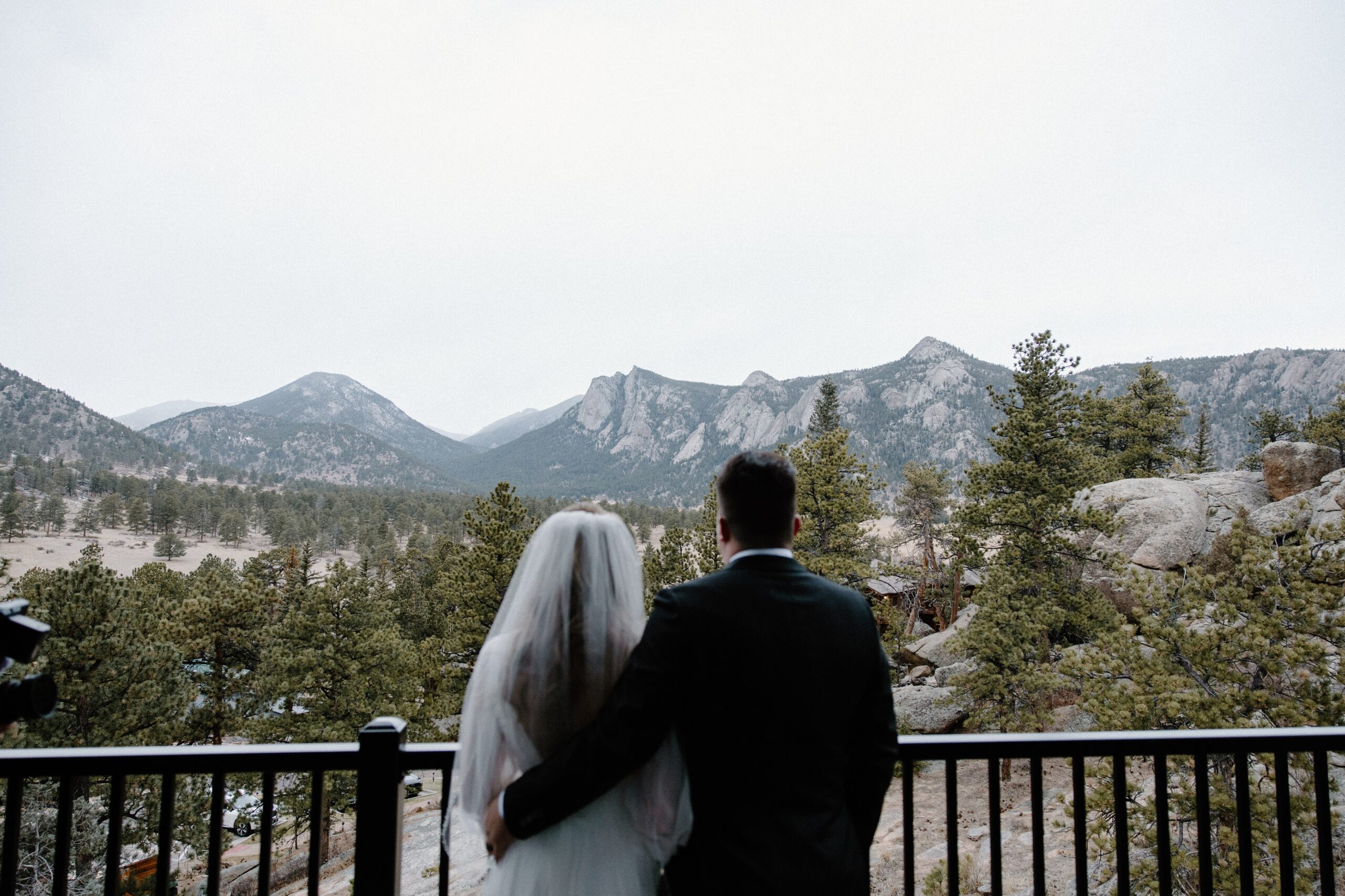 A couple standing shoulder to shoulder in wedding attire looking out over the mountains during their Estes Park wedding in Colorado