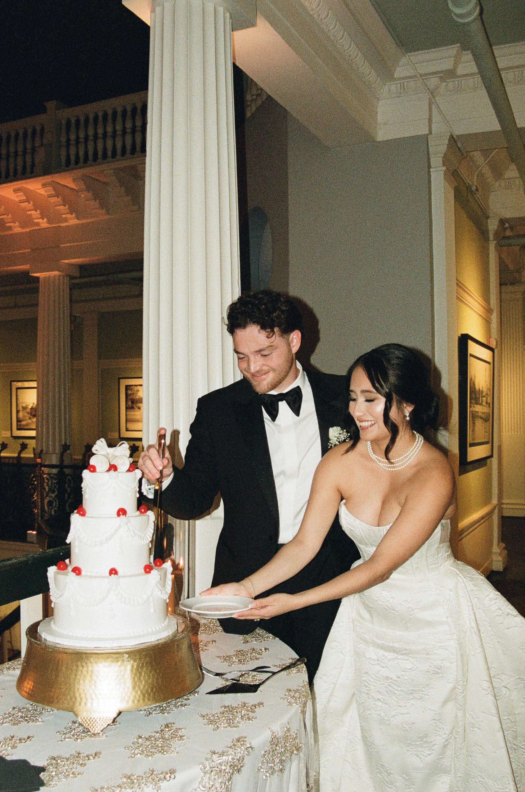 A newlywed couple, cutting their wedding cake as they both smile and the woman holds out a plate caption on 35 mm film in Florida