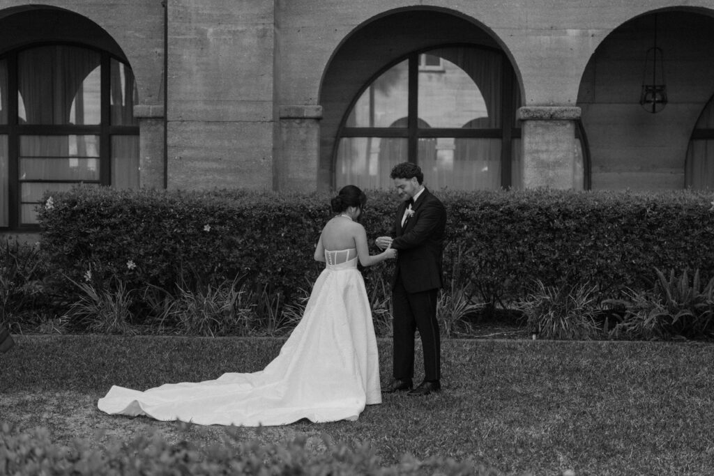 A couple in wedding attire looking at each others wedding outfits during their first look in St. Augustine during their big wedding