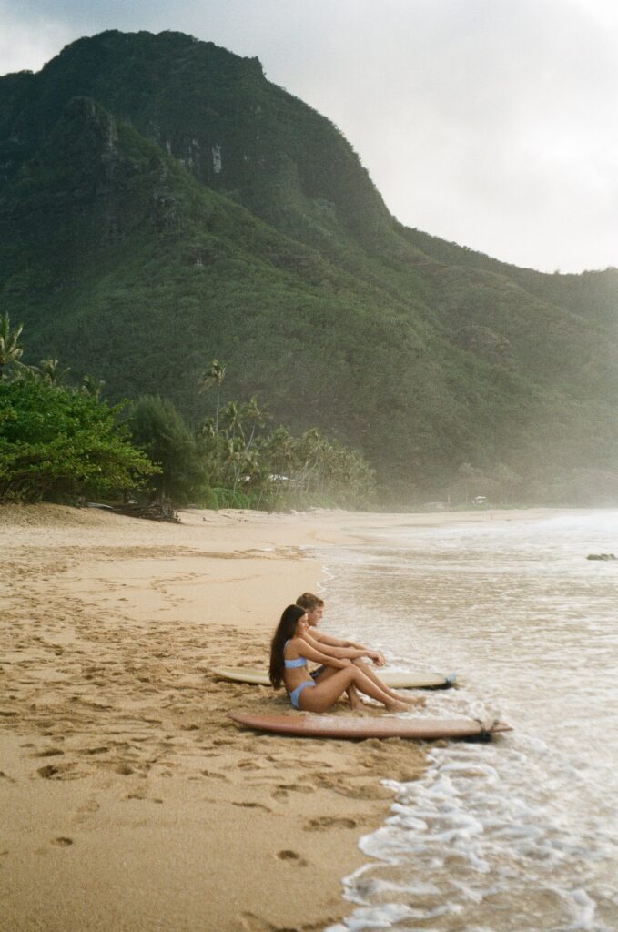 A couple sitting on a beach in Hawaii after surfing on their adventure elopement day adventure elopement ideas