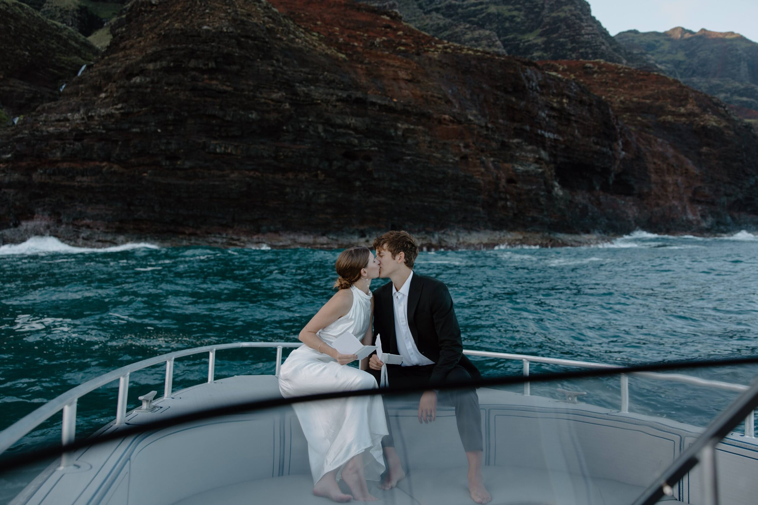 A couple sharing a case on the front of a boat, with a big fuse behind them during their sunrise wedding on Kauai