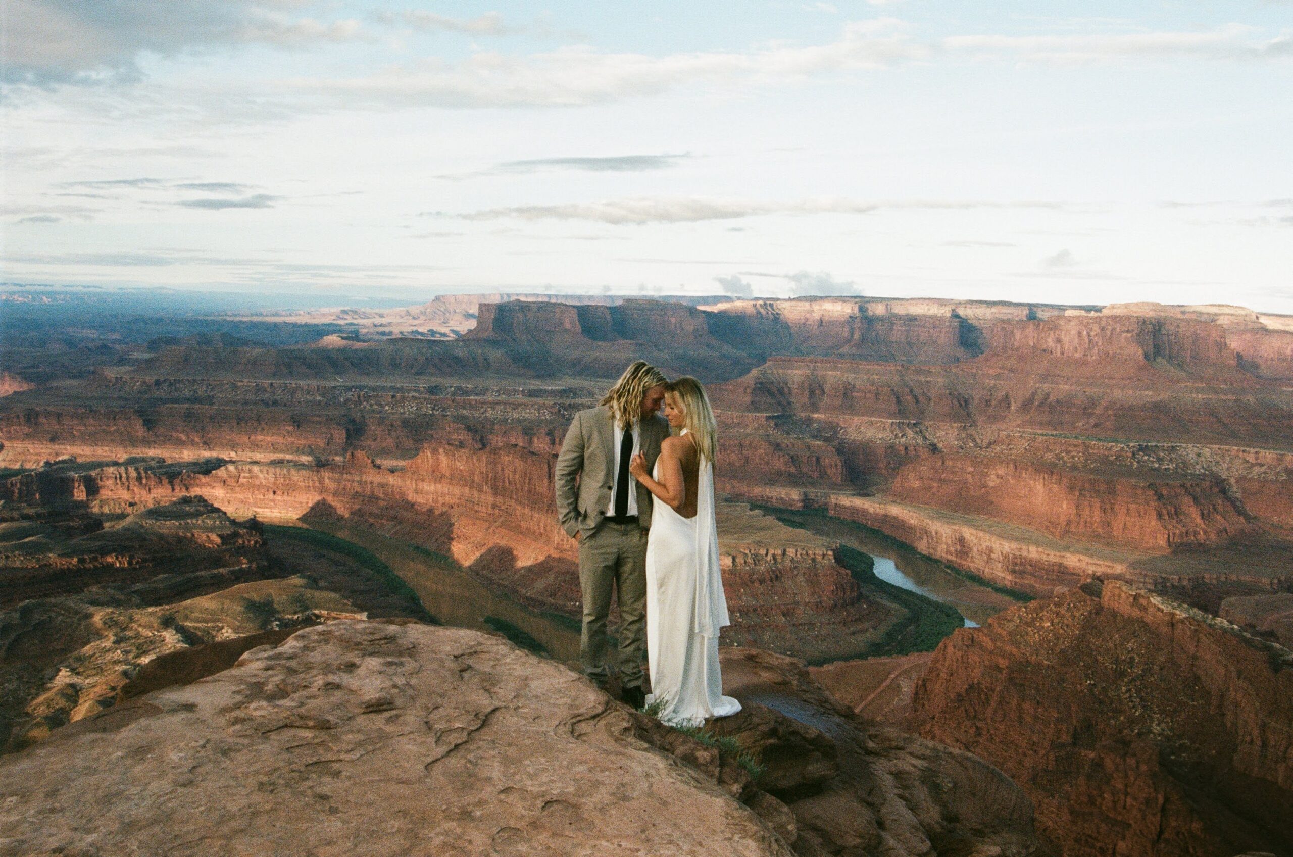 A couple standing with their foreheads press together in wedding attire on a cliff in Deadhorse State Park, during their sunrise, adventure elopement in Utah
