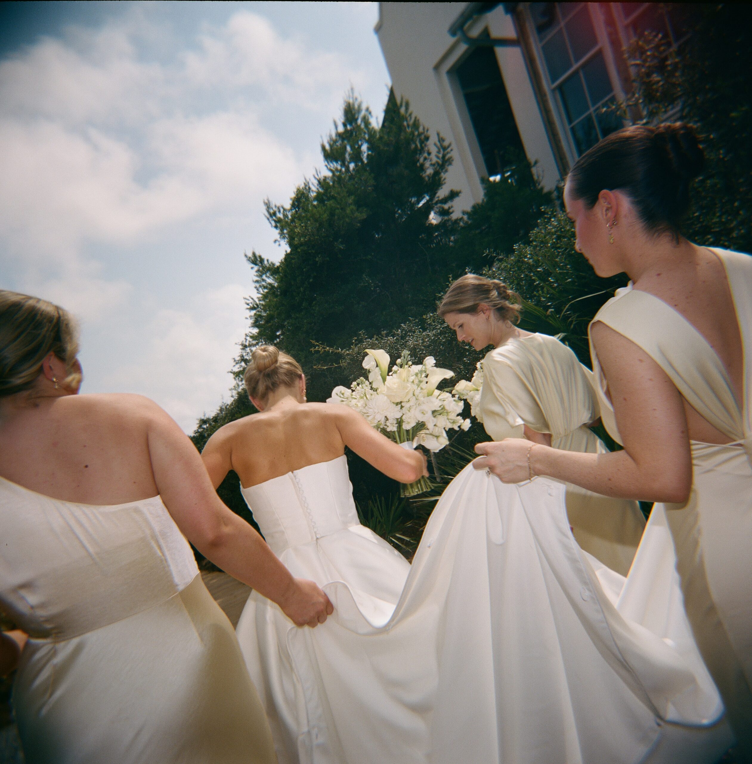 A woman walking along a boardwalk as her bridesmaids and yellow dresses hold up her dress during her destination wedding in Rosemary Beach, Florida