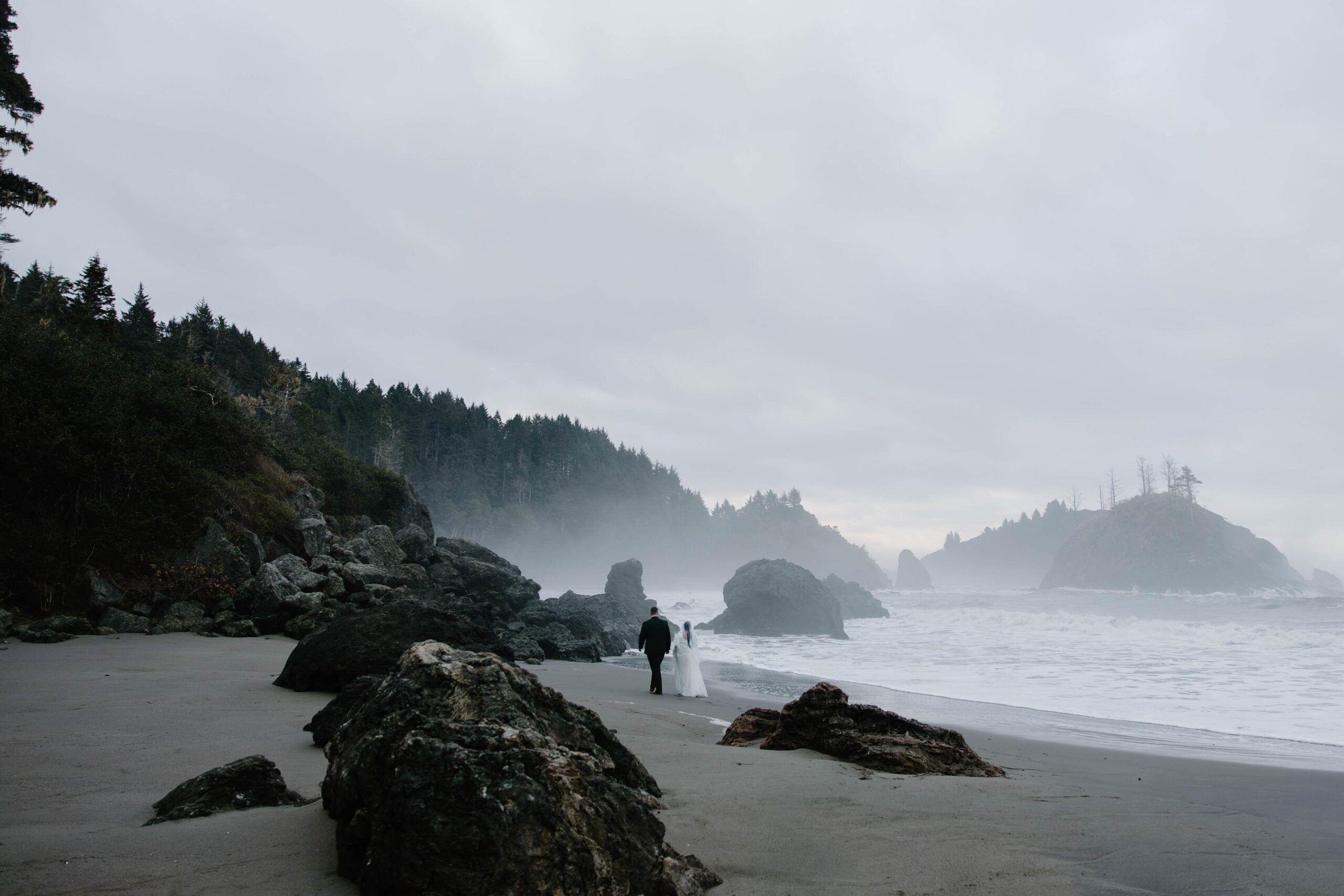 Bride and groom walking along the rocky shoreline at sunrise in Trinidad.