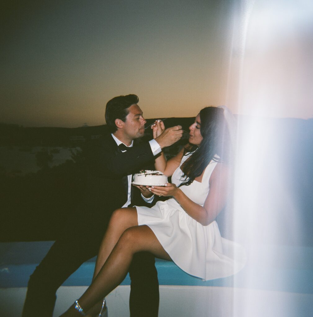 A couple feeding each other cake as the sun sets during their Greece Elopement on Milos Island