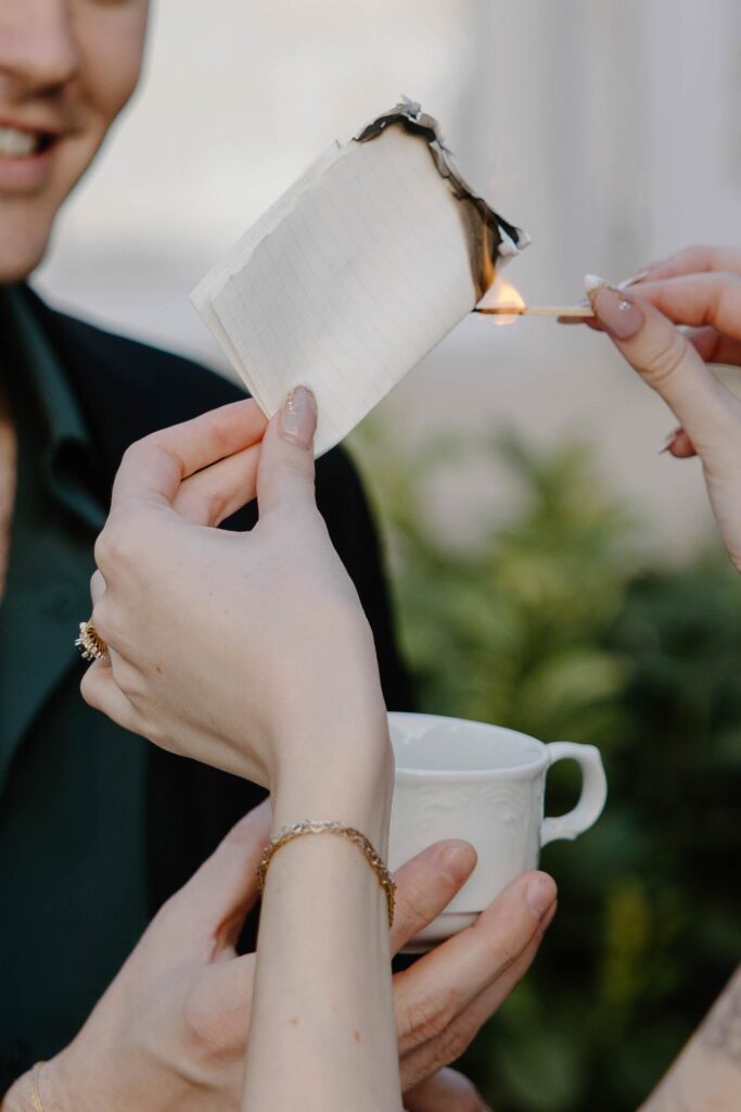 A woman holding a match and lighting paper on fire during burning of intentions during their fall elopement in Europe