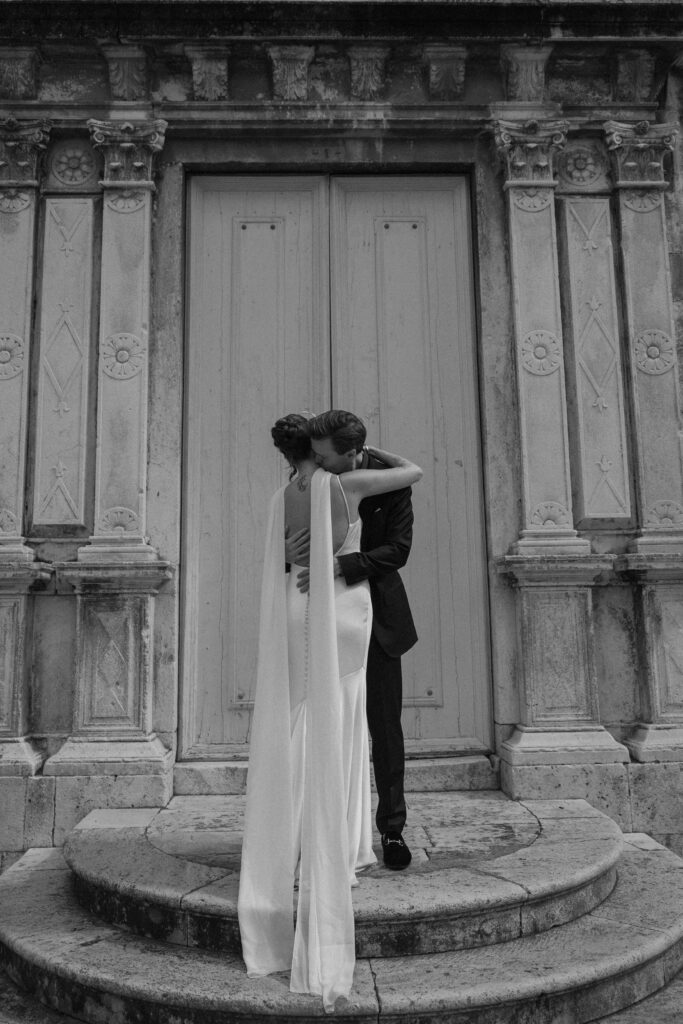 Bride and groom embracing in front of ornate historic church doors in Hvar, Croatia.
