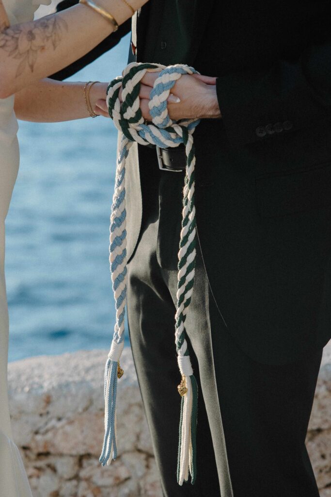 Close-up of couple holding hands after their hand-fasting ceremony with the Adriatic Sea in the background during their elopement.
