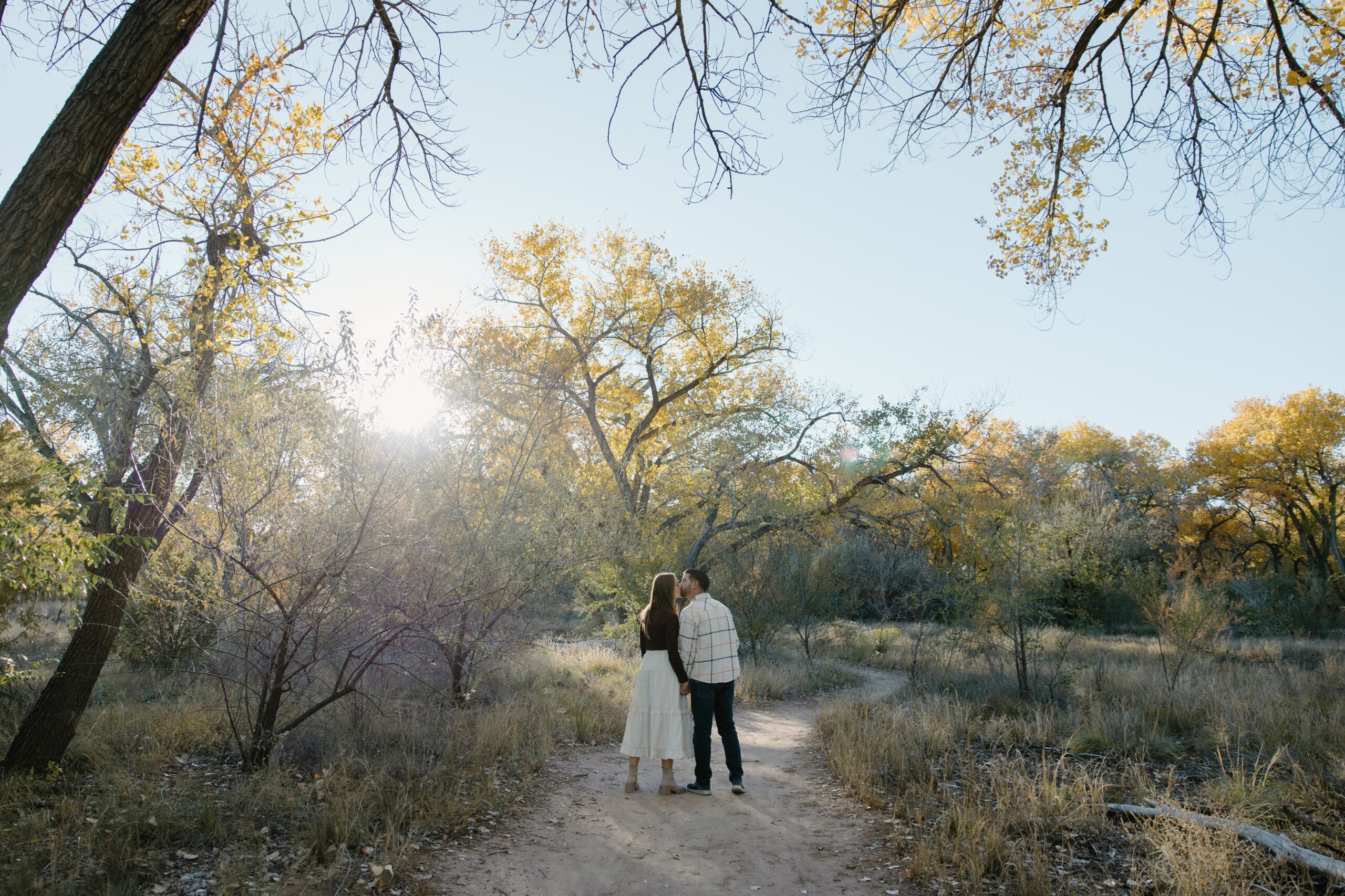 Max and Jenny sharing a kiss while surrounded by golden autumn trees in Albuquerque.