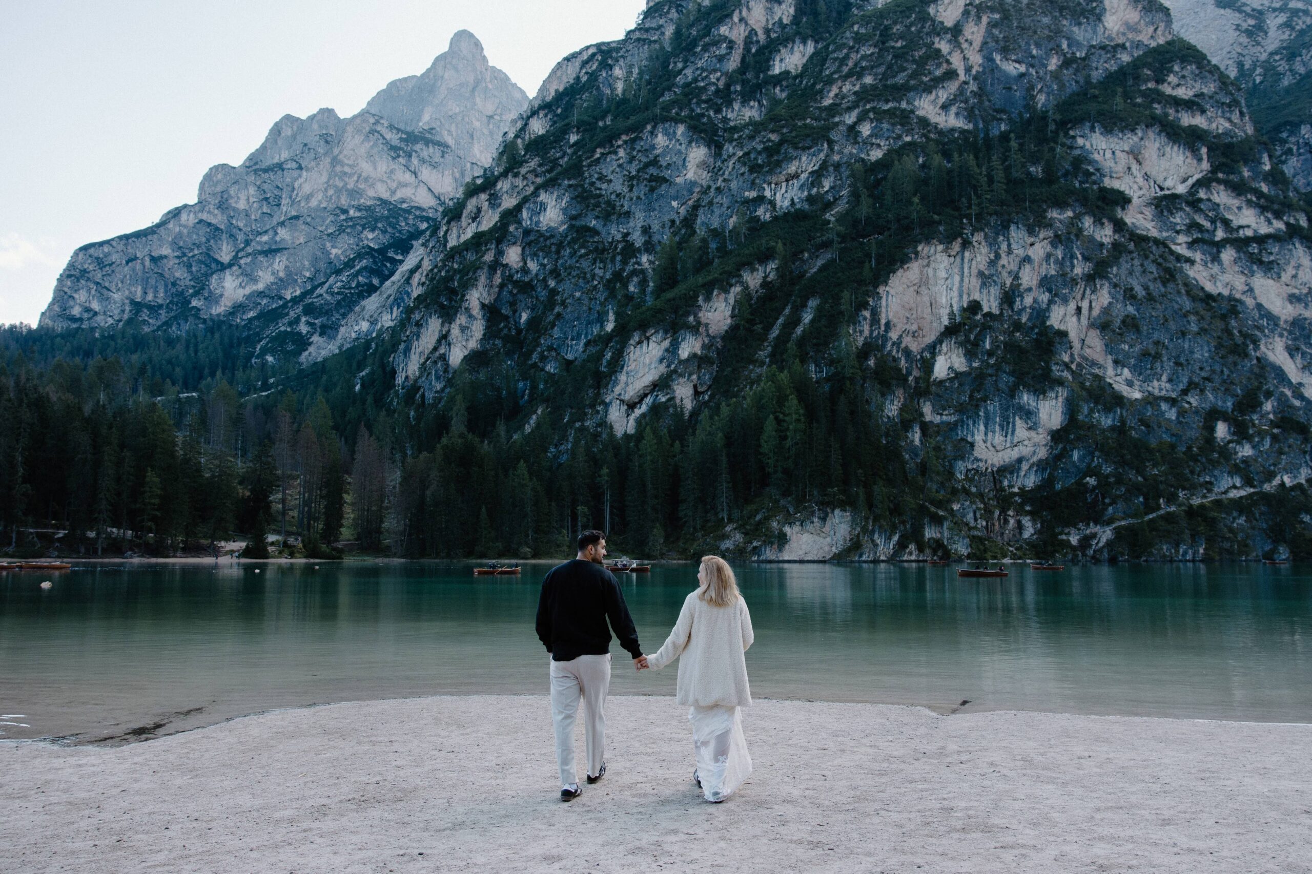 A couple in wedding attire walking towards a mountain with snow on it during their lake elopement in Italy