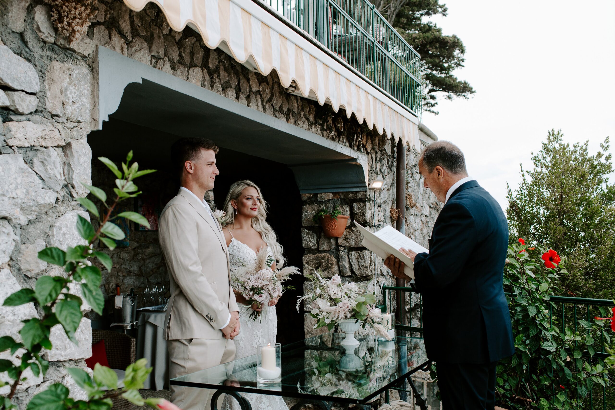 A couple in wedding attire standing on a balcony with their officiant during their Capri, Italy elopement