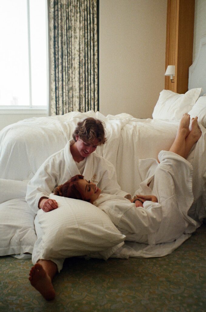 A couple sitting on the hotel floor in robes as they laugh during their NOLA elopement on film