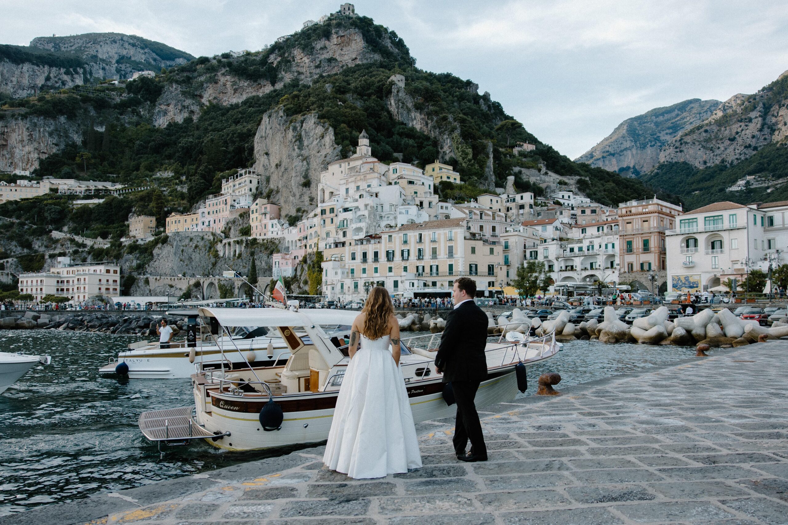 A couple in wedding attire standing along the docks on the Amalfi Coast during their fall elopement