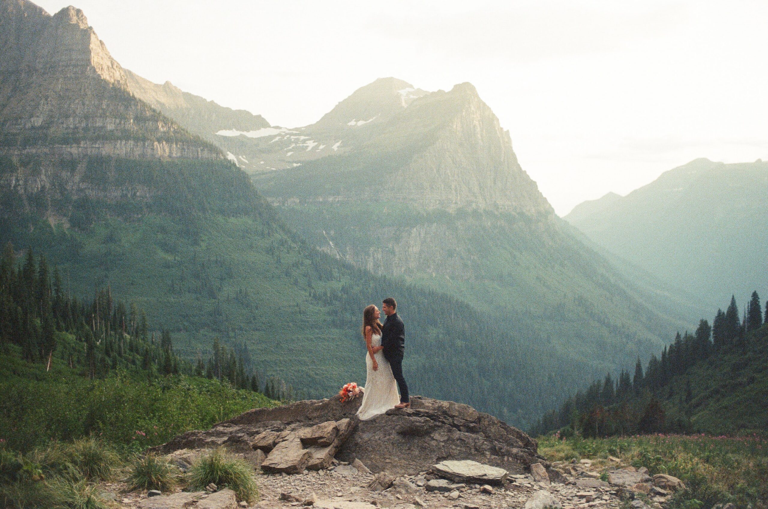 A couple embracing as they stand on a rock during their Glacier National Park elopement