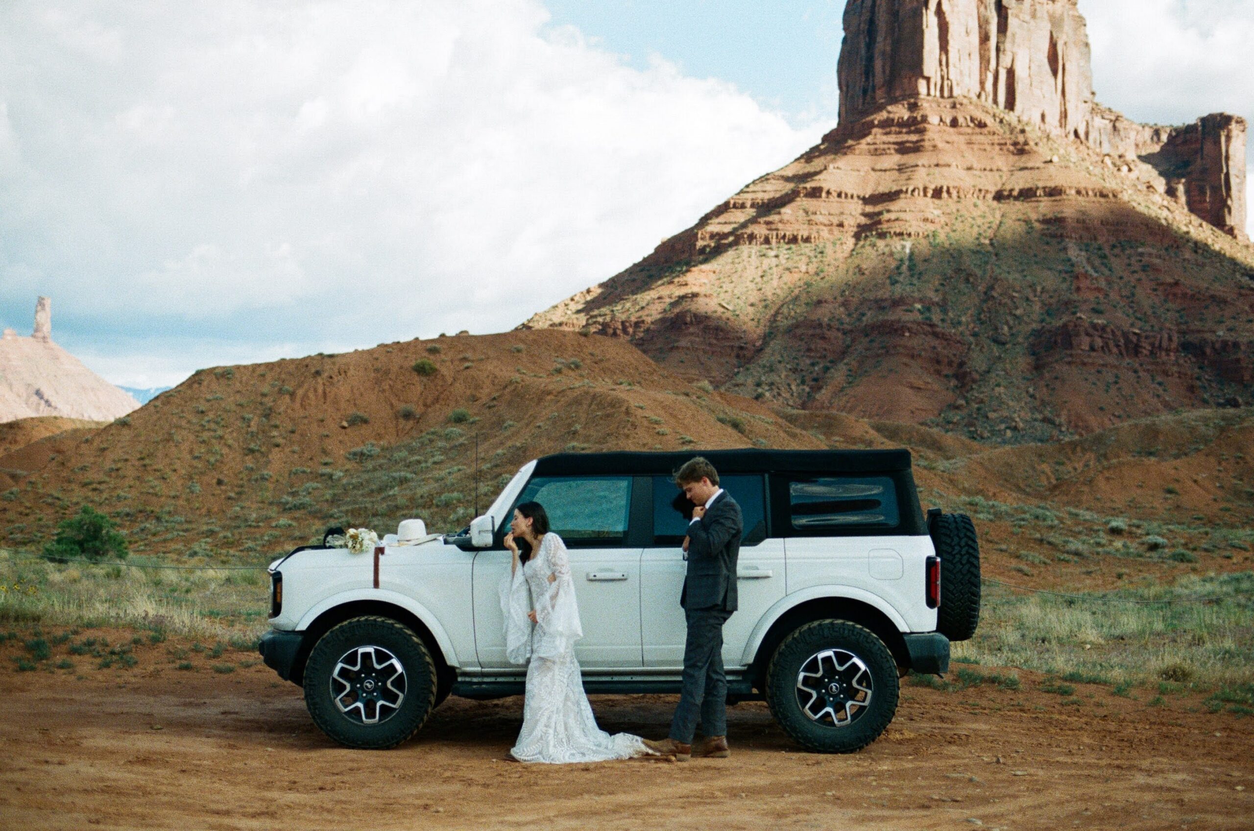 Couple standing beside Bronco during desert elopement on BLM land outside of Moab Utah as they get ready