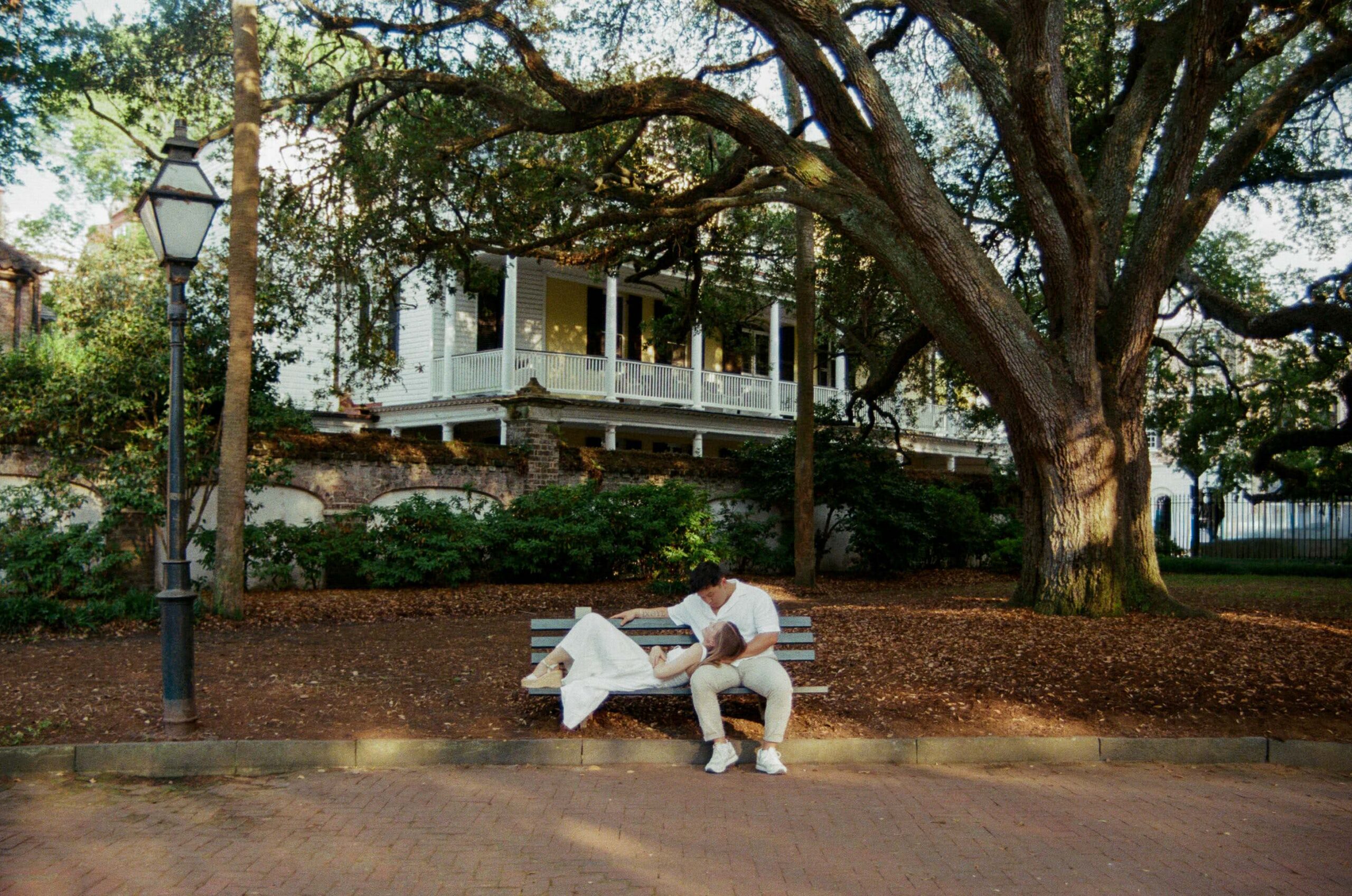 Couple sitting beneath moss covered oak trees in Downtown Charleston during a spring engagement photography session on 35mm film