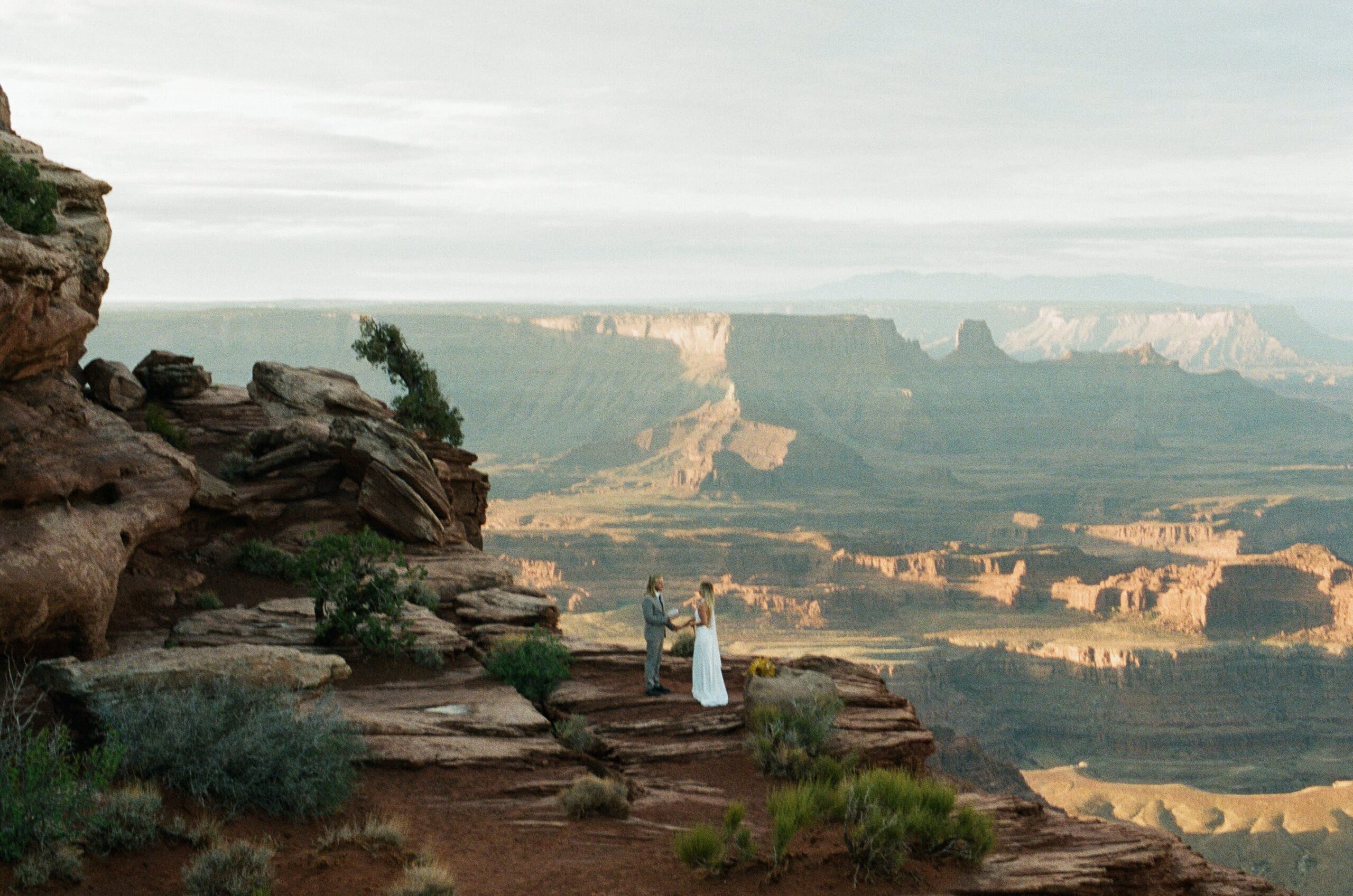 Bride and groom standing on a canyon overlook during a Dead Horse Point sunrise elopement photographed on film.